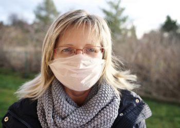 Eine blonder Frau mit Brille trägt einen Mundschutz.