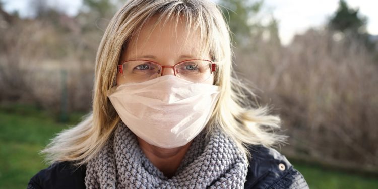 Eine blonder Frau mit Brille trägt einen Mundschutz.