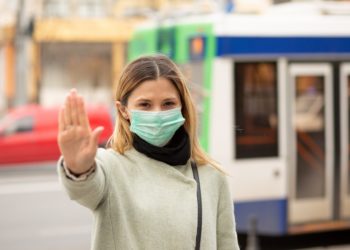 Frau mit medizinischer Gesichtsmaske macht mit der Hand das Zeichen, von ihr weg zu bleiben