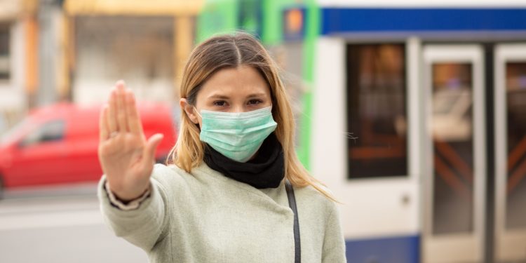 Frau mit medizinischer Gesichtsmaske macht mit der Hand das Zeichen, von ihr weg zu bleiben