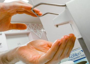 Ein Paar Hände bedienen einen Desinfektionsmittel-Spender in einem Krankenhaus.