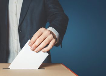 Mann steckt einen Wahlzettel in eine Wahlurne