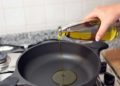 Aus einer durchsichtigen Flasche wird Speieseöl in eine Pfanne auf einem Herd geschüttet