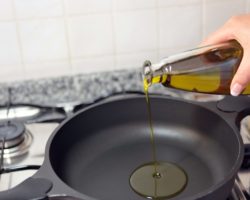 Aus einer durchsichtigen Flasche wird Speieseöl in eine Pfanne auf einem Herd geschüttet