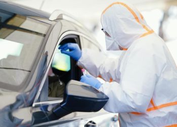 Eine Person im Schutzanzug kontrolliert ein Auto.
