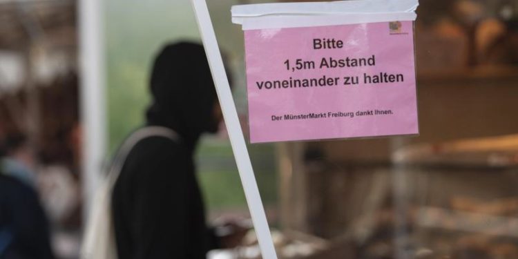 Ein Mann kauft auf dem Markt ein. Am Stand ist ein Schild angebracht mit der Aufschrift «Bitte 1,5 m Abstand voneinander zu halten».