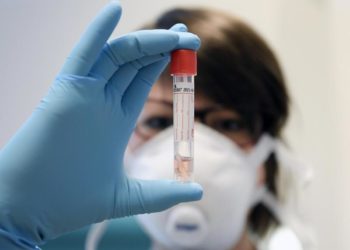 Eine Wissenschaftlerin hält ein Röhrchen vor sich.