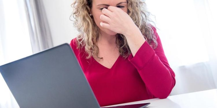 Eine Frau sitzt vor einem Laptop und reibt sich die Augen.