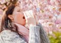 Niesende Frau vor rosa blühendem Baum