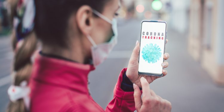 Eine Frau mit Mund-Nasen-Schutz schaut auf ihr Smartphone.