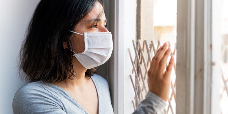 June Frau mit Mund-Nasen-Schutz sieht aus dem Fenster