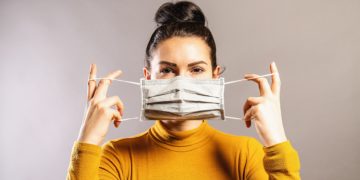 Junge Frau legt eine Mundschutzmaske an