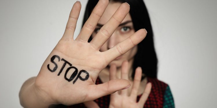 Frau hält ihre rechte Handfläche vor das Gesicht, auf der STOP geschrieben steht