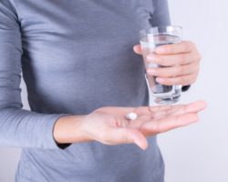 Frau hält in einer Hand ein Glas Wasser und in der anderen zwei Tabletten