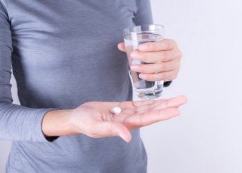 Frau hält in einer Hand ein Glas Wasser und in der anderen zwei Tabletten