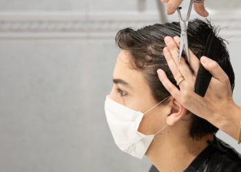 Einem Jugendlichen mit Mund-Nasen-Bedeckung werden die Haare geschnitten