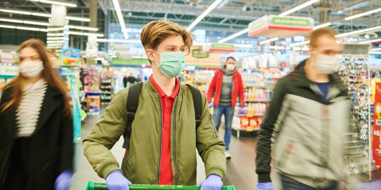 Mann mit Schutzmaske, Handschuhen und einem Einkaufswagen im Supermarkt