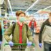 Mann mit Schutzmaske, Handschuhen und einem Einkaufswagen im Supermarkt
