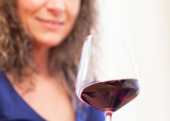 Eine Frau hält ein Glas mit Rotwein in der Hand.