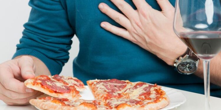 Ein Mann fasst sich auf die Brust, während er eine Pizza isst.