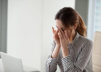 Müde Frau im Büro massiert ihre Nasenwurzel