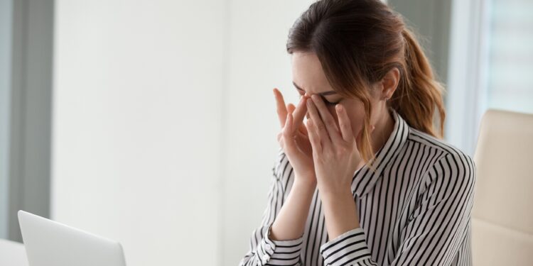 Müde Frau im Büro massiert ihre Nasenwurzel