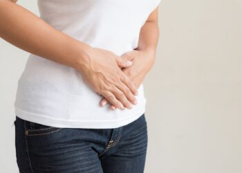 Eine Frau in Jeans und weißem T-Shirt hält sich die Hände auf den Bauch.