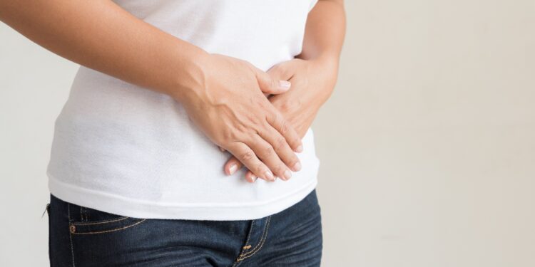 Eine Frau in Jeans und weißem T-Shirt hält sich die Hände auf den Bauch.