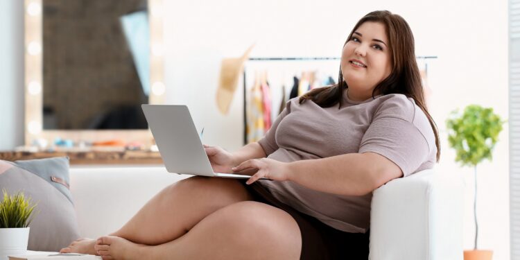 Übergewichtige Frausitzt mit Laptop auf dem Sofa