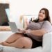 Übergewichtige Frausitzt mit Laptop auf dem Sofa