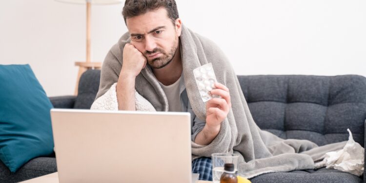 Ein kränklich aussehender Mann schaut auf einen Laptop.