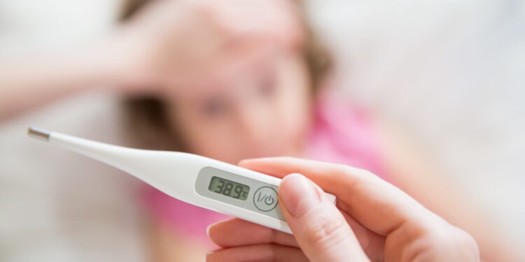 Mutter misst mit Fieberthermometer die Temperatur ihrer Tochter und hält die Hand an die Stirn des Mädchens