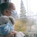 Ein junge mit Mund-Nasen-Schutzmaske sitzt am Fenster.