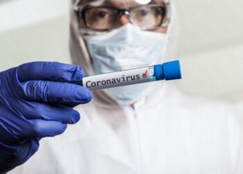 Arzt mit Gesichtsmaske und Handschuhen hält ein Reagenzglas mit einem Coronavirus-Test