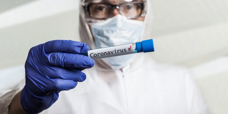 Arzt mit Gesichtsmaske und Handschuhen hält ein Reagenzglas mit einem Coronavirus-Test