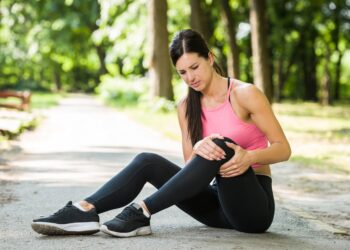 Läuferin sitzt im Park auf dem Boden und hält ihr schmerzendes Knie