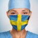 Eine Frau trägt eine Mund-Nasenschutzmaske in den Farben der schwedischen Flagge.