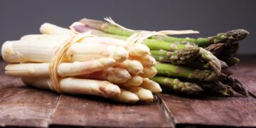 Ein Bund weißer Spargel und ein Bund grüner Spargel auf einem Holztisch