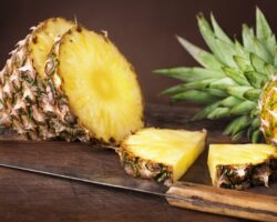 Geschnittene und ganze Ananas und ein Messer auf einem Holztisch