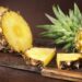 Geschnittene und ganze Ananas und ein Messer auf einem Holztisch