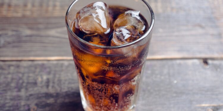 Ein mit Cola und Eiswürfeln gefülltes Glas auf einem Holztisch