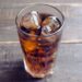 Ein mit Cola und Eiswürfeln gefülltes Glas auf einem Holztisch
