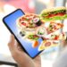 Grafische Darstellung eines Smartphones, aus dem ungesunde Lebensmittel wie Pizza und Burger herausfliegen.