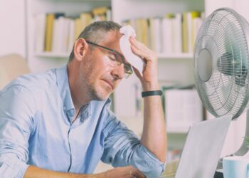 Mann im Homeoffice leidet unter Hitze und versucht, sich durch einen Ventilator abzukühlen