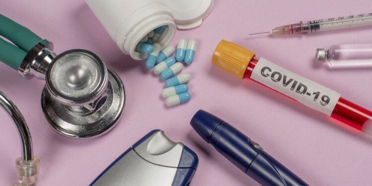 Eine Blutprobe mit der Aufschrift "COVID-19" liegt neben medizinischen Gegenständen, die bei Diabetes zum Einsatz kommen.