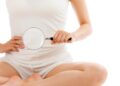 Frau im Schneidersitz hält eine Vergrößerungslupe vor ihrem Bauch