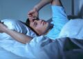 Junger Mann mit Einschlafproblemen liegt nachts wach im Bett