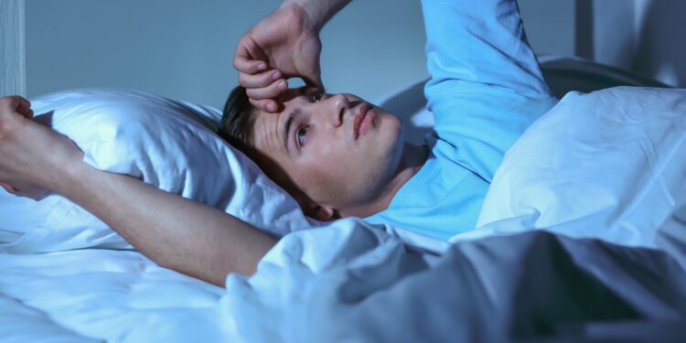 Junger Mann mit Einschlafproblemen liegt nachts wach im Bett