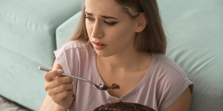 Eine Frau mit unglücklichem Gesichtsausdruck isst einen Schokoladenkuchen.
