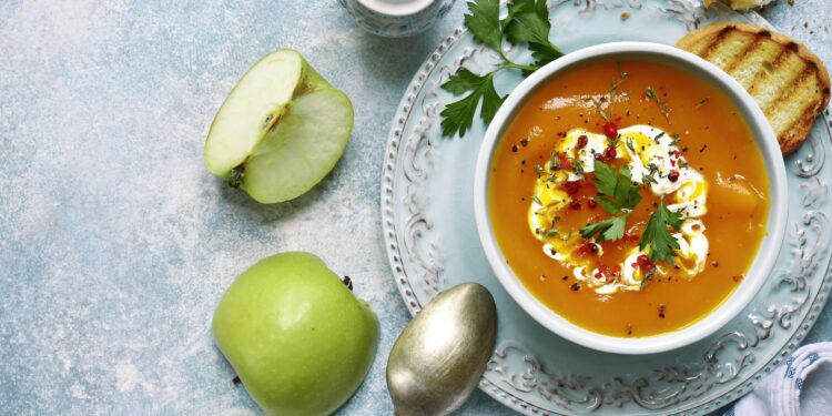 Eine Möhrensuppe wird auf einer weißen Oberfläche präsentiert.